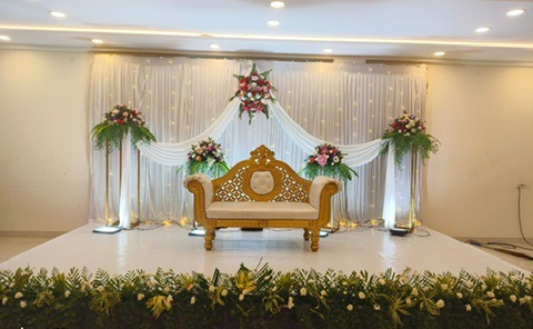 Wedding reception stage with white drapes and green floral border at VJK Mahal, Pallavaram Chennai